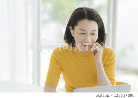 イヤホンをつけてノートパソコンに向かうアラフィフの女性 128517896
