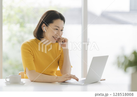イヤホンをつけてノートパソコンに向かうアラフィフの女性 イヤホンをつけてノートパソコンに向かうアラフィフの女性 128518008