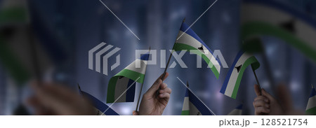 Lesotho flags in their hands on a blurred urban background Lesotho flags in their hands on a blurred urban background 128521754