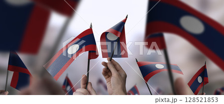 Laos flags in their hands on a blurred urban background Laos flags in their hands on a blurred urban background 128521853