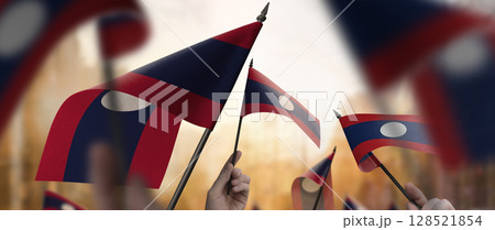 Laos flags in their hands on a blurred urban background Laos flags in their hands on a blurred urban background 128521854