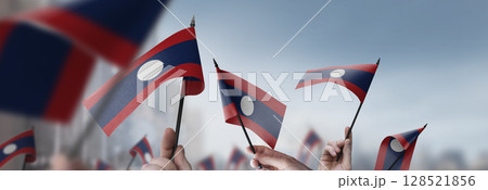 Laos flags in their hands on a blurred urban background 128521856