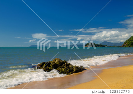 A serene scene at Trinity Beach, with crystal-clear waters of the Coral Sea, framed by lush tropical greenery, just north of Cairns in Far North Queensland, Australia A serene scene at Trinity Beach, with crystal-clear waters of the Coral Sea, framed by lush tropical greenery, just north of Cairns in Far North Queensland, Australia 128522776