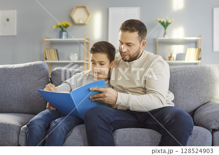Father And Son Reading Book Together On Couch During Leisure Time At Home 128524903