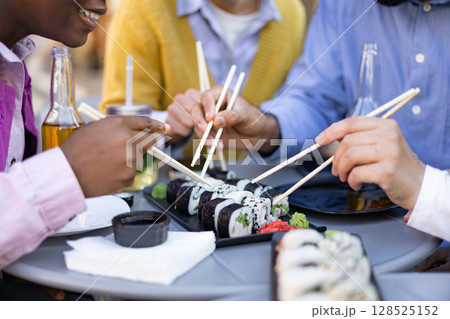 Friends sharing a meal of sushi and drinks at an outdoor restaurant, enjoying the delicious Japanese cuisine. 128525152