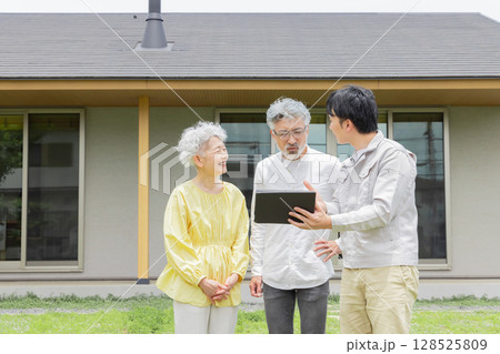住宅の前で説明する男性作業員とシニア夫婦 住宅の前で説明する男性作業員とシニア夫婦 128525809