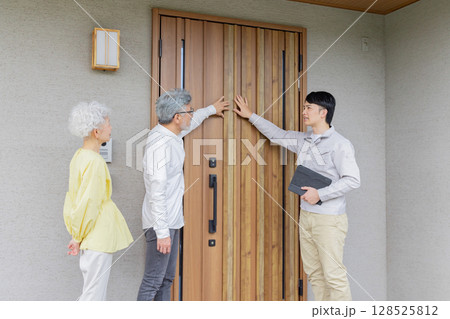 住宅の前で説明する男性作業員とシニア夫婦 住宅の前で説明する男性作業員とシニア夫婦 128525812