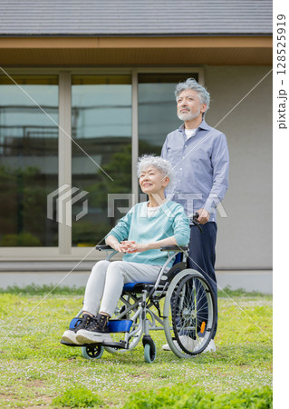 住宅の前を歩く車椅子に乗ったシニア夫婦 住宅の前を歩く車椅子に乗ったシニア夫婦 128525919