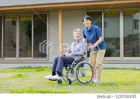 住宅の前で車椅子に乗ったシニア男性と介護士 住宅の前で車椅子に乗ったシニア男性と介護士 128526193