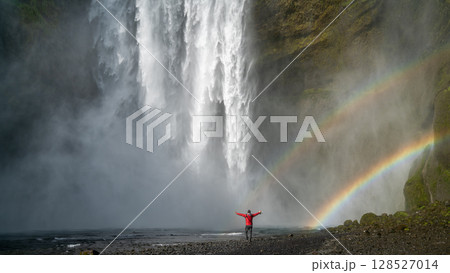 Unidentified woman stands beneath the powerful Skogafoss waterfall in Iceland, framed by mist and a vivid rainbow Unidentified woman stands beneath the powerful Skogafoss waterfall in Iceland, framed by mist and a vivid rainbow 128527014