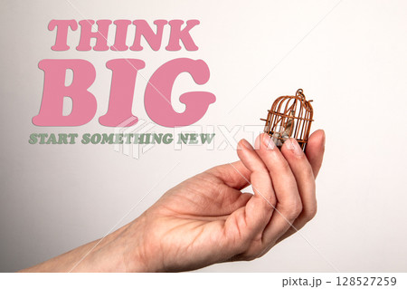 Think Big. Miniature Birdcage Held in Hand on Light Background Think Big. Miniature Birdcage Held in Hand on Light Background 128527259
