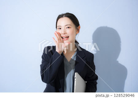 パソコン持ってスーツを着た立つ応援声援、内緒など呼びかける、若いかわいい女性のビジネス上半身 水色 パソコン持ってスーツを着た立つ応援声援、内緒など呼びかける、若いかわいい女性のビジネス上半身 水色 128529046