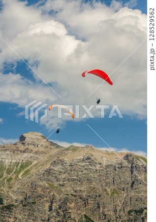 Paragliders Soaring Over Rocky Alpine Peaks Under Blue Sky and White Clouds. High quality photo 128529562