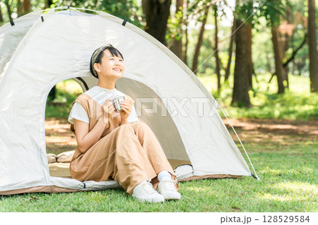 キャンプ場・レジャー施設でテントの前でドリンクを飲む女の子 128529584