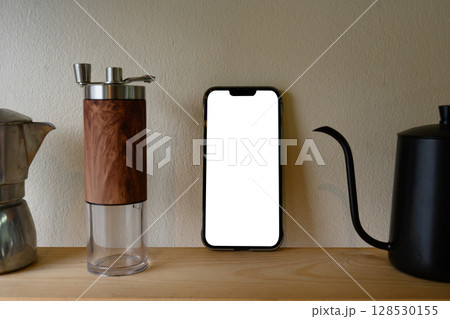 Blank smartphone screen on a wooden shelf next to manual coffee equipment 128530155