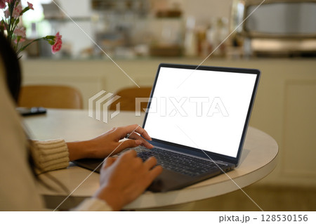 Female hands typing on a laptop with a white empty screen at a cafe table Female hands typing on a laptop with a white empty screen at a cafe table 128530156