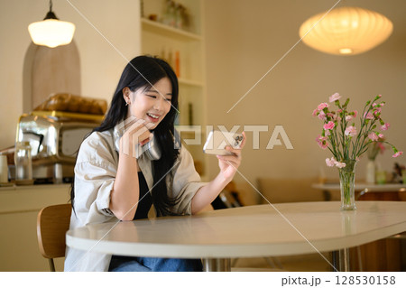 Relaxed Asian female using her smartphone, seated in a trendy coffee shop Relaxed Asian female using her smartphone, seated in a trendy coffee shop 128530158