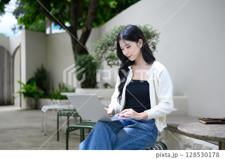 Pretty young woman working on her laptop in a peaceful outdoor cafe Pretty young woman working on her laptop in a peaceful outdoor cafe 128530178