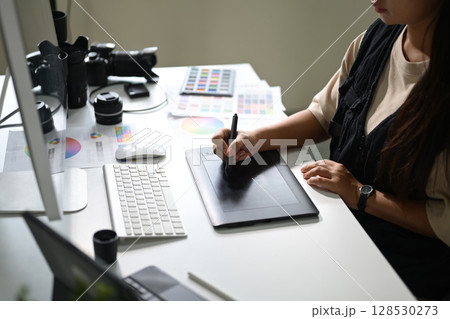Photographer retouching images on a graphic tablet at a workstation Photographer retouching images on a graphic tablet at a workstation 128530273