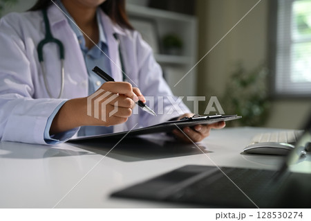 Close up of female doctor filling out patient information or notes during consultation online 128530274