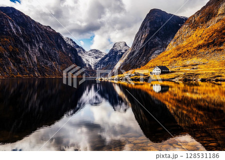 Reflection of mountain and house in calm fjord waters in Norway, showcasing serene natural landscape and peaceful atmosphere Reflection of mountain and house in calm fjord waters in Norway, showcasing serene natural landscape and peaceful atmosphere 128531186