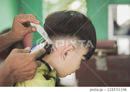 Barber Trimming Boy's Hair with Scissors and Comb in Barbershop 128531196