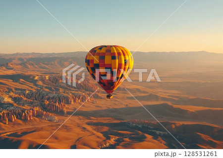 Hot air balloon flying over desert dunes at sunrise with warm glowing sky and peaceful atmosphere 128531261