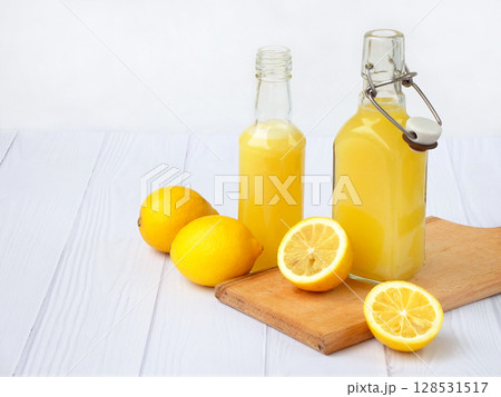 Freshly squeezed lemon juice in bottle and lemons on light background. For vitamin drink or cocktail. Selective focus. Space for text Freshly squeezed lemon juice in bottle and lemons on light background. For vitamin drink or cocktail. Selective focus. Space for text 128531517