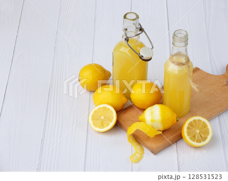Freshly squeezed lemon juice in bottle and lemons on light background. For vitamin drink or cocktail. Selective focus. Space for text. Freshly squeezed lemon juice in bottle and lemons on light background. For vitamin drink or cocktail. Selective focus. Space for text. 128531523