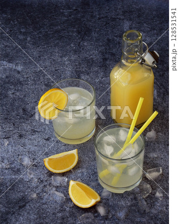 glasses of cold homemade lemonade with lemon slices, ice cubes and straws on dark background. Copy space 128531541
