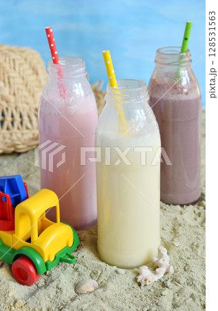 Three bottle of various milkshakes chocolate, strawberry and vanilla . Healthy smoothie with straw. Tasty milk shake cocktails. Refreshing summer drink on yellow sand summer beach. Copy space. 128531563