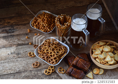 Football fan set with mugs of beer and salty snacks on wooden background. Crackers, pretzel, salted straws, nuts, dried fish. Junk food for beer or cola. Photographed with natural light. Football fan set with mugs of beer and salty snacks on wooden background. Crackers, pretzel, salted straws, nuts, dried fish. Junk food for beer or cola. Photographed with natural light. 128531583