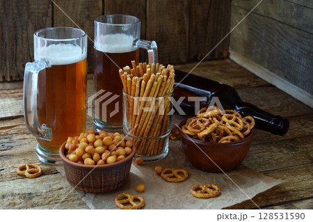 Football fan set with mugs of beer, bottle and salty snacks on wooden background. Crackers, pretzel, salted straws, nuts, dried fish. Junk food for beer or cola. Photographed with natural light Football fan set with mugs of beer, bottle and salty snacks on wooden background. Crackers, pretzel, salted straws, nuts, dried fish. Junk food for beer or cola. Photographed with natural light 128531590
