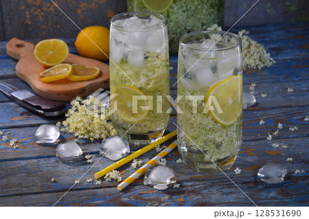 Elderberry flowers and lemon drink. Refreshing healthy summer juice. Glass of elderflower lemonade on wooden rustic board. Alternative medicine and therapy. Elderberry flowers and lemon drink. Refreshing healthy summer juice. Glass of elderflower lemonade on wooden rustic board. Alternative medicine and therapy. 128531690