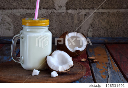 Coconut milk in bottle with broken coco on wooden background. Delicious milk cocktail. Copy space Coconut milk in bottle with broken coco on wooden background. Delicious milk cocktail. Copy space 128531691