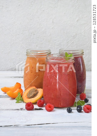 Orange, red and purple healthy smoothies of fresh ingredients - bananas, apricots, raspberries and blueberries on a light background. Copy space Orange, red and purple healthy smoothies of fresh ingredients - bananas, apricots, raspberries and blueberries on a light background. Copy space 128531723