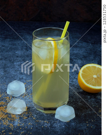 One glass of cold homemade lemonade with lemon slices, ice cubes, brown sugar and straws on dark background. Copy space One glass of cold homemade lemonade with lemon slices, ice cubes, brown sugar and straws on dark background. Copy space 128531750