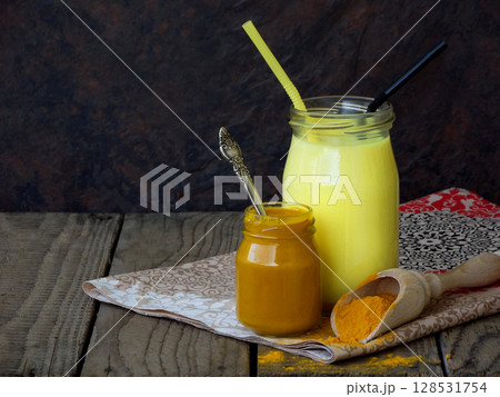 Turmeric powder, paste and latte on wooden background. Ayurvedic healthy golden drink with coconut milk and ghee for beauty and health. Selective focus. Copy space 128531754