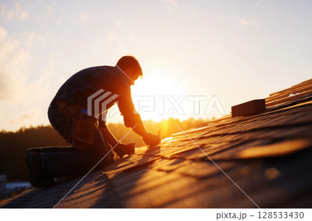 A close-up image of a home repair, focusing on a roofer installing shingles on a roof. 128533430