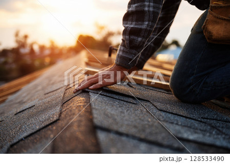 A close-up image of a home repair, focusing on a roofer installing shingles on a roof. A close-up image of a home repair, focusing on a roofer installing shingles on a roof. 128533490