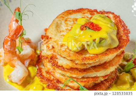 Crispy potato pancakes stacked with creamy yellow curry sauce, garnished with shrimp, herbs, and red caviar pearls 128533835