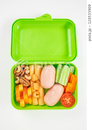 Bright green lunchbox filled with sausages, cheese, nuts, fruits, and fresh vegetables including cucumber, carrot, and tomato, organized in a colorful and nutritious arrangement Bright green lunchbox filled with sausages, cheese, nuts, fruits, and fresh vegetables including cucumber, carrot, and tomato, organized in a colorful and nutritious arrangement 128533909