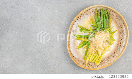 Elegant plate of sauteed green and white asparagus topped with grated cheese and fresh herbs, served in a creamy butter sauce on a speckled ceramic dish 128533923