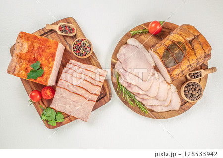 A delicious assortment of smoked and cooked meats is beautifully arranged on wooden boards with herbs, spices, and fresh vegetables, ideal for showcasing traditional deli or charcuterie products A delicious assortment of smoked and cooked meats is beautifully arranged on wooden boards with herbs, spices, and fresh vegetables, ideal for showcasing traditional deli or charcuterie products 128533942