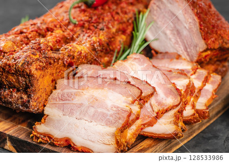 Close-up of juicy sliced pork belly with a spicy red crust, showcasing its marbled texture and rich seasoning on a rustic wooden board Close-up of juicy sliced pork belly with a spicy red crust, showcasing its marbled texture and rich seasoning on a rustic wooden board 128533986