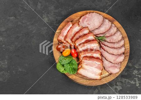 A wooden serving board with a mix of sliced smoked pork and spicy pork belly, garnished with cherry tomatoes, spinach leaves, and rosemary A wooden serving board with a mix of sliced smoked pork and spicy pork belly, garnished with cherry tomatoes, spinach leaves, and rosemary 128533989
