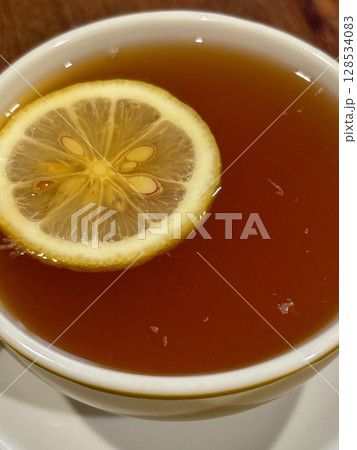 Close up of a full cup of English tea, with a slice of lemon floating on top. Close up of a full cup of English tea, with a slice of lemon floating on top. 128534083