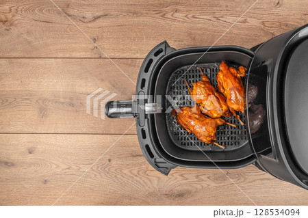 Three perfectly roasted quails with golden, crispy skin are arranged inside an air fryer basket, ready to serve on a wooden background Three perfectly roasted quails with golden, crispy skin are arranged inside an air fryer basket, ready to serve on a wooden background 128534094
