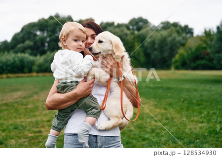 Beautiful woman is standing on the field and holding puppy and little boy Beautiful woman is standing on the field and holding puppy and little boy 128534930