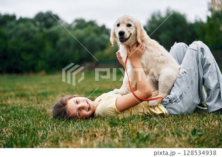 On the ground. Cute little girl is with golden retriever dog on the field 128534938